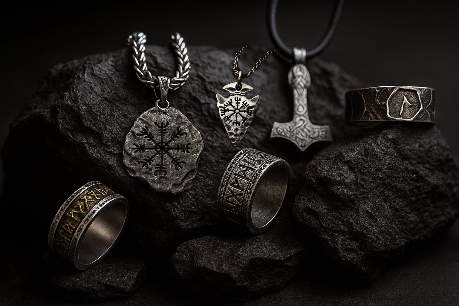 Wikinger Schmuck auf schwarzem Felsen – Runenschmuck von NORDSKULLS mit Thorshammer, Vegvisir und Runenringen im nordischen Stil.