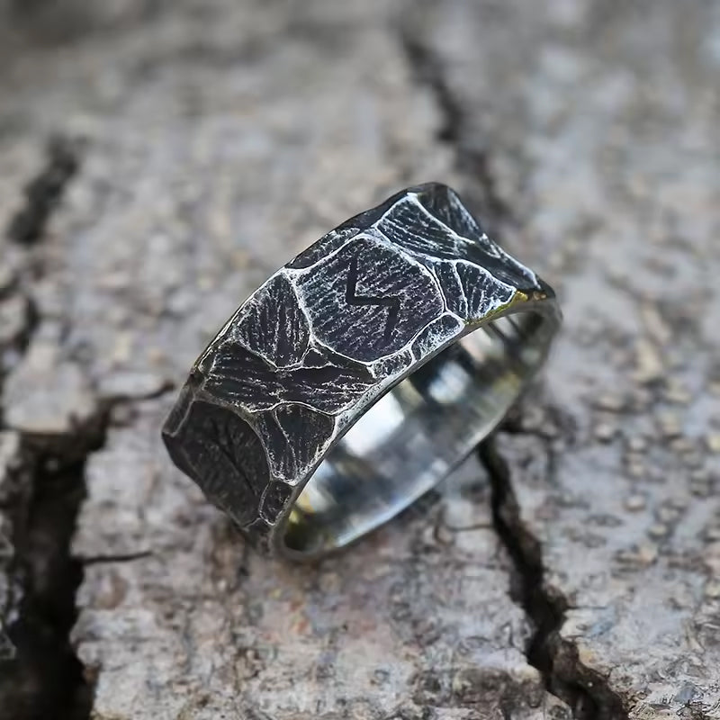 Runen Ring aus Edelstahl mit eingravierten Runen – liegend auf Baumrinde im natürlichen Wikinger-Stil – gehämmerte, antik wirkende Oberfläche mit symbolischer Gravur – kraftvoller, hochwertiger Wikinger Runenschmuck von NORDSKULLS.