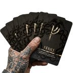 Wikinger Tarot Karten Elder Futhark Runen Orakel – Hand mit Wikinger Tattoo hält Runenkarte FEHU aus nordischem Runen Orakel Deck, Wahrsagekarten inspiriert von Wikinger Mythologie und Runenmagie